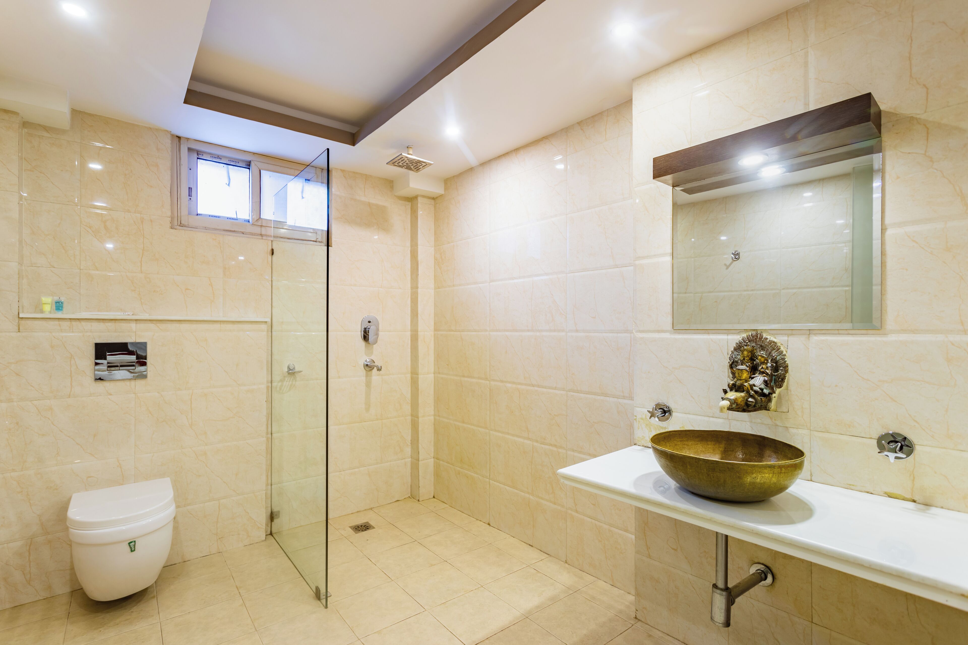 A modern bathroom with a glass shower enclosure, a white toilet, and a large gold bowl sink.