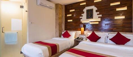 A hotel room with two beds, a wooden headboard, a small bedside table, and a glass shower enclosure.