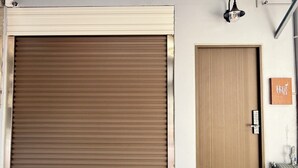 A closed roller door with a brown finish, a wooden door next to it, and a small sign with Chinese characters. - Linshouse (Tainan)