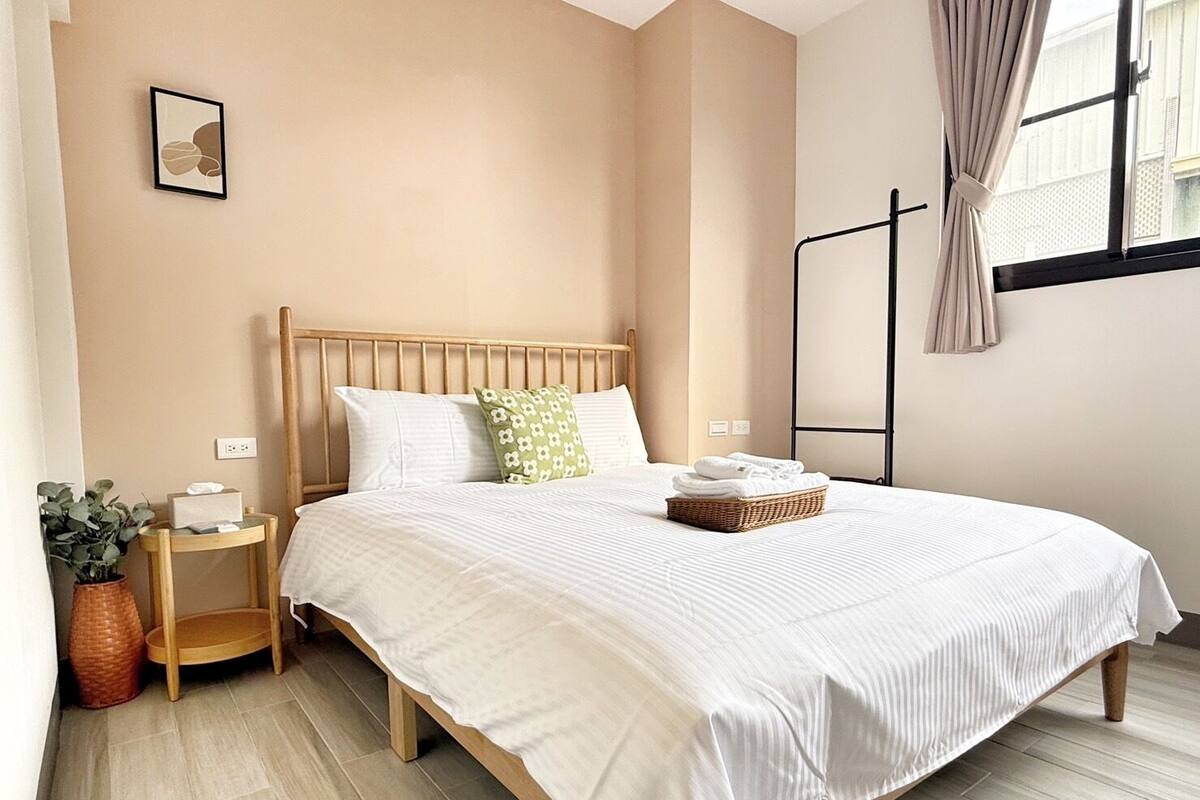 Uma cama bem arrumada com cabeceira de madeira, mesa de cabeceira com abajur e janela com cortinas.