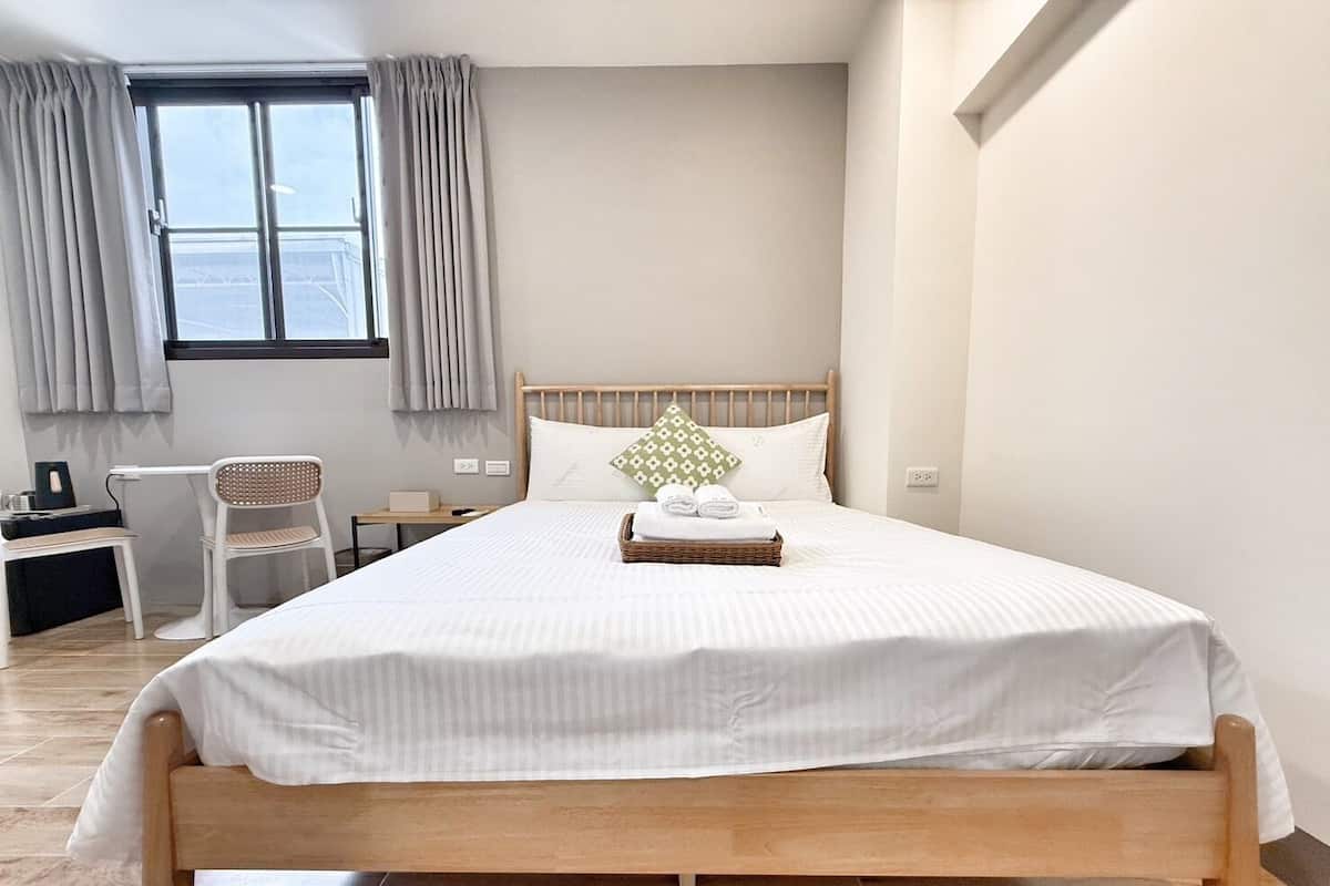 Quarto bem arrumado com uma cama de madeira, uma secretária pequena e uma cadeira, com uma janela e cortinas.