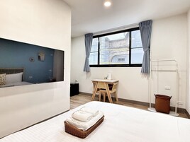 Une chambre d’hôtel avec un lit, un bureau, une chaise, une fenêtre avec des rideaux et une petite poubelle.