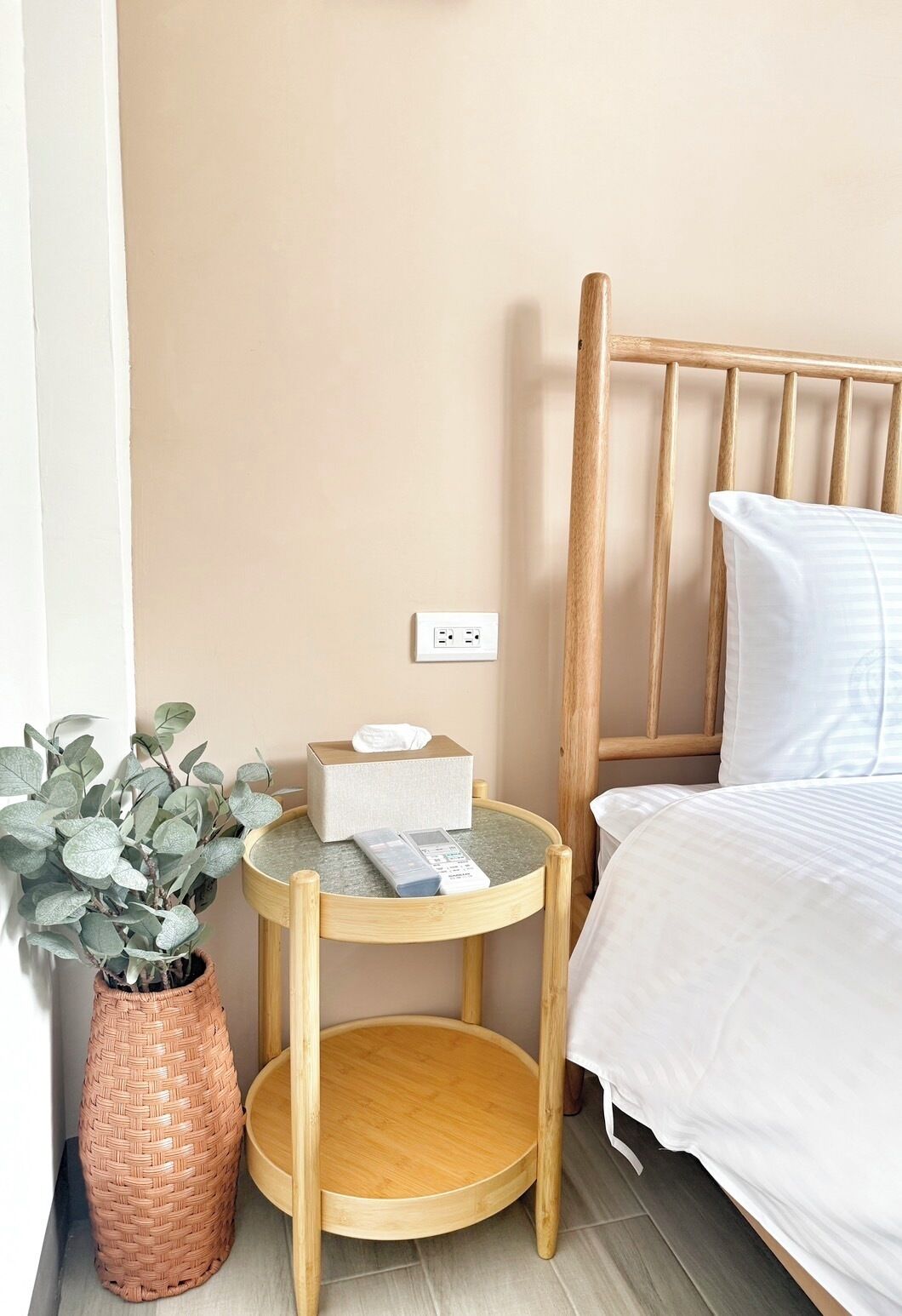 A neatly arranged bedroom with a wooden bed, a bedside table with a remote control, a tissue box, and a potted plant.
