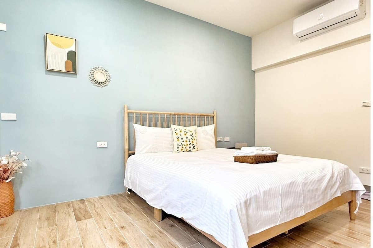Um quarto com cama de madeira, roupa de cama branca, um objeto decorativo pequeno na parede e um cesto de vime sobre a cama.