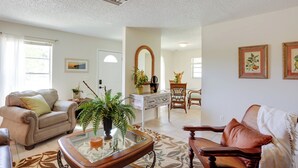 Una sala de estar con sofá, sillón, mesa de centro y una zona de comedor con una silla y una mesa.