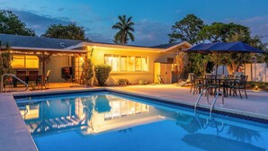 Zona de piscina con piscina, mobiliario exterior y un edificio con luces colgantes.