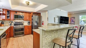 Una cocina moderna con armarios de madera, electrodomésticos de acero inoxidable, una isla de piedra con taburetes y un ventanal grande.
