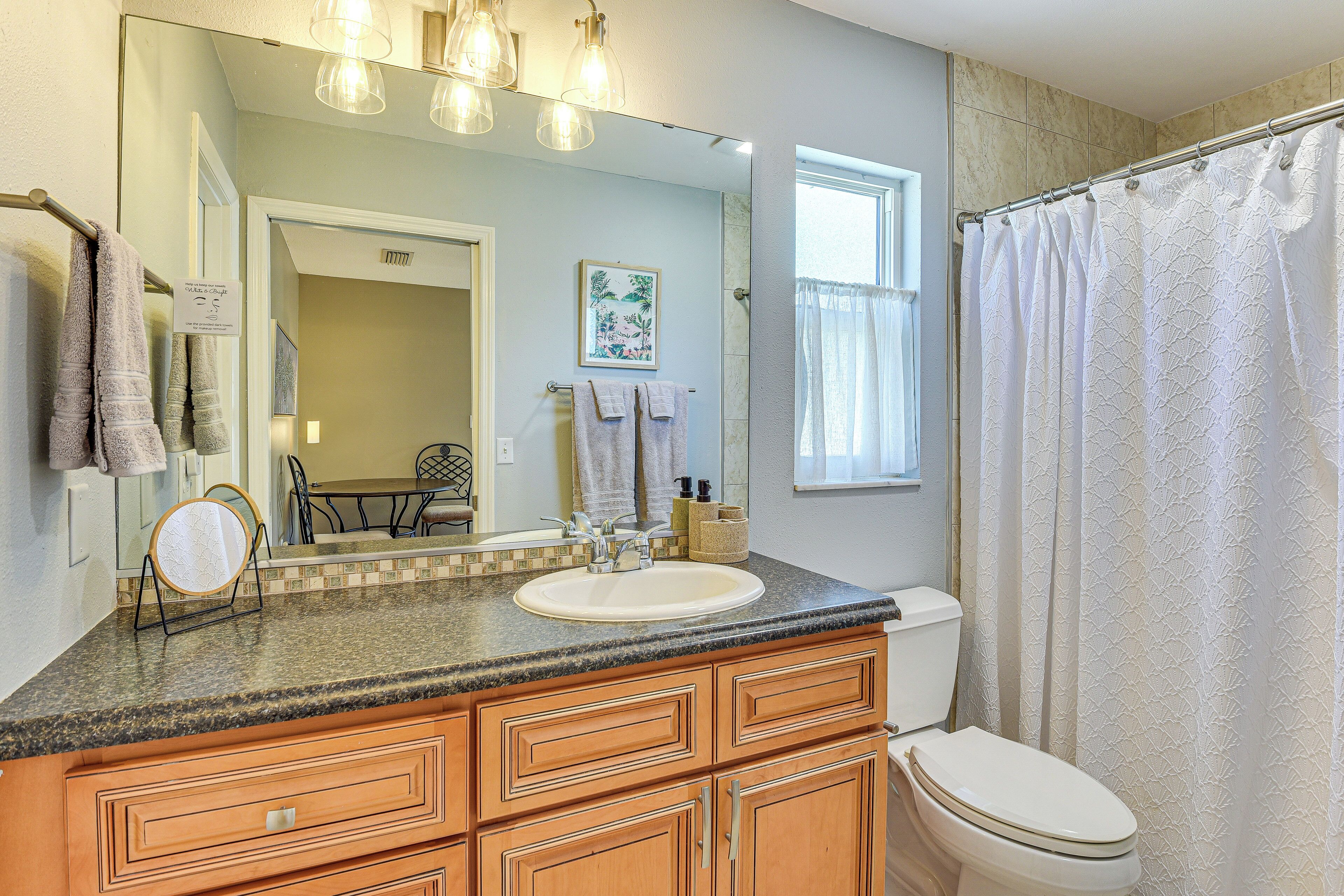 A bathroom with a granite countertop, wooden cabinetry, a white sink, a toilet, and a shower curtain.