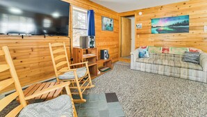 Een gezellig interieur van een chalet met houten details, een grote flatscreen televisie, een bank en een schommelstoel.
