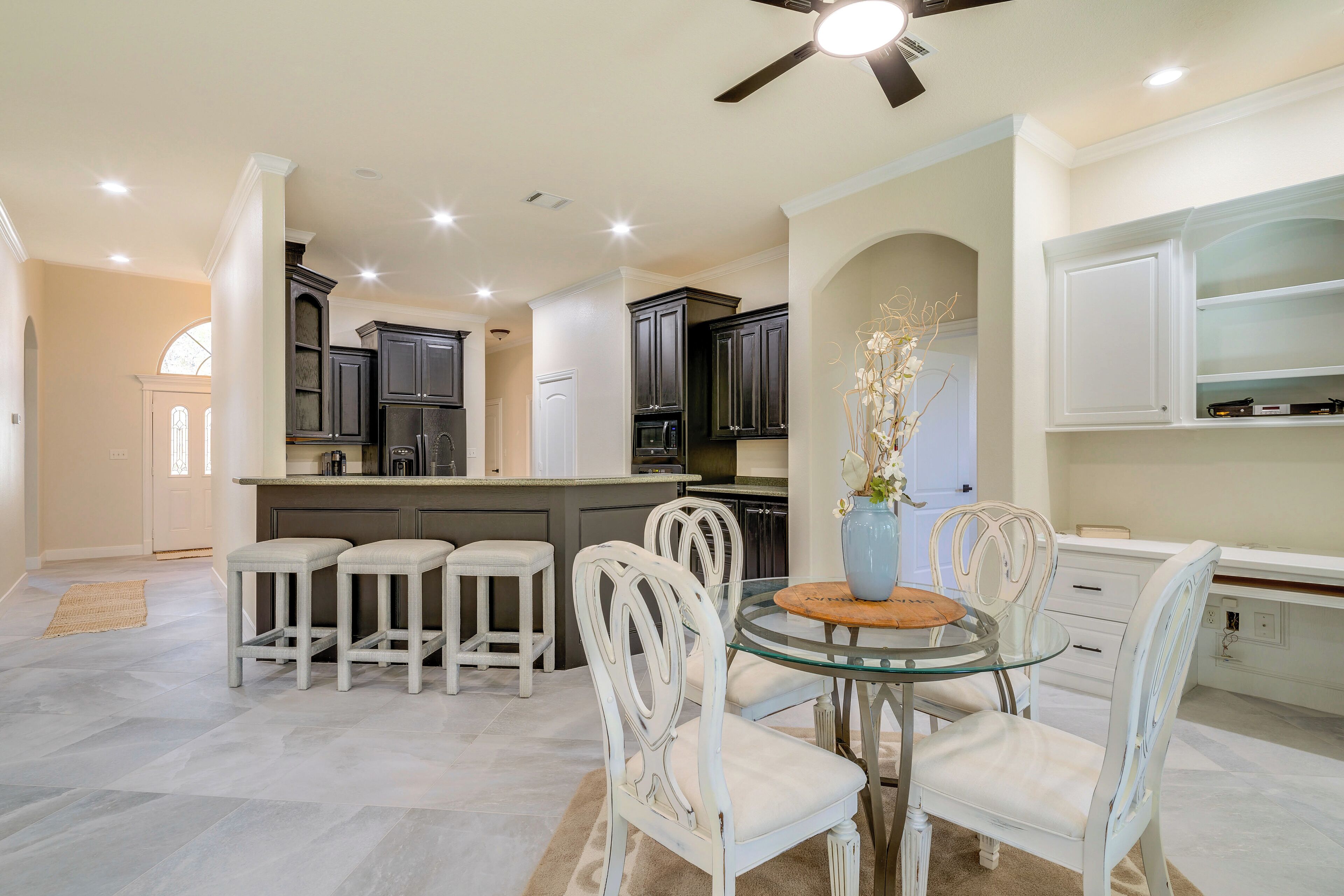 A modern kitchen with white cabinetry, a glass dining table, and a ceiling fan.
