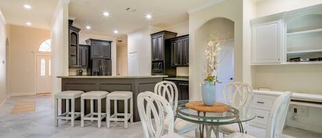 A modern kitchen with white cabinetry, a glass dining table, and a ceiling fan.