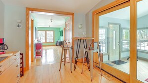 Um quarto espaçoso com piso de madeira, área de jantar com duas cadeiras, uma mesa e vista através de uma porta de vidro.