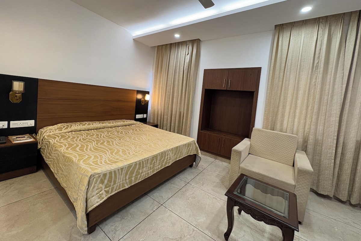 Quarto de hotel com cama, cadeira, televisão, guarda-roupa e ventoinha no teto.