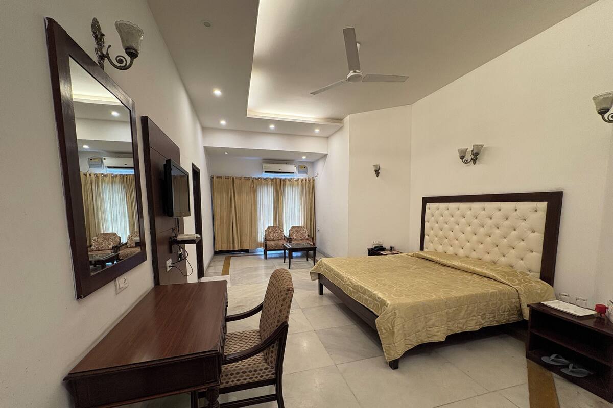 Quarto de hotel com cama, escrivaninha, cadeira, televisão e ventoinha no teto.