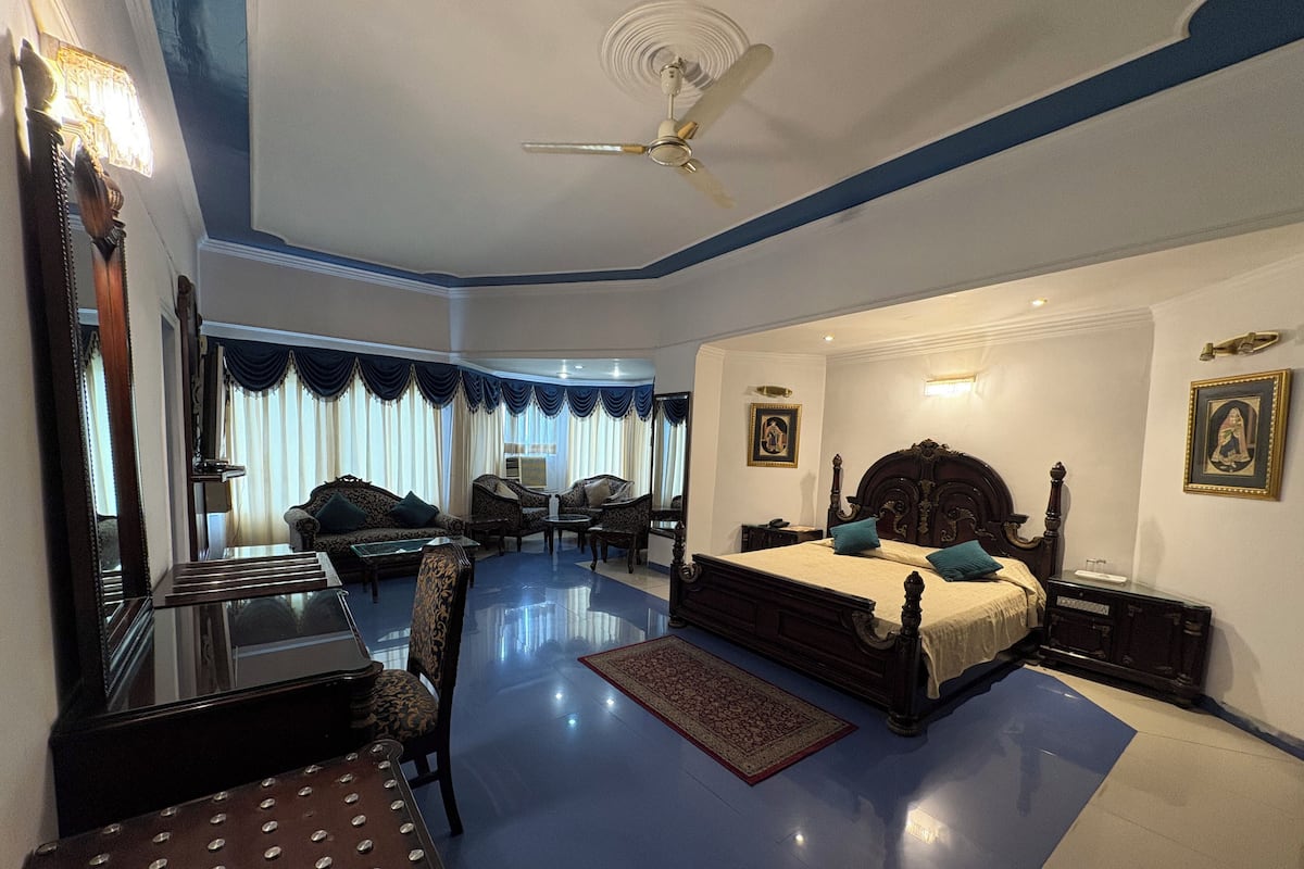 Quarto com uma cama grande, ventilador de teto, área de estar com cadeiras, mesa de centro e um espelho grande.