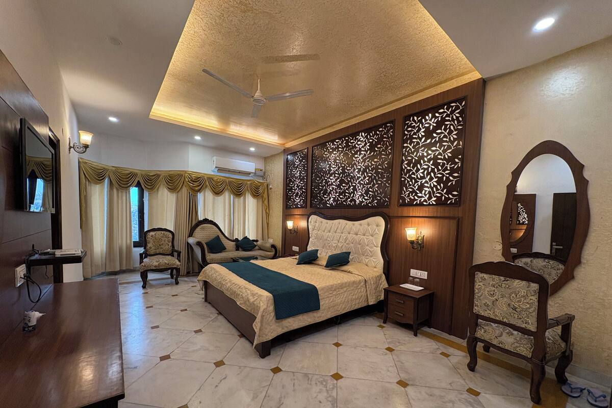 Quarto de hotel com cama, escrivaninha, cadeira, televisão, ventoinha no teto e painéis decorativos nas paredes.