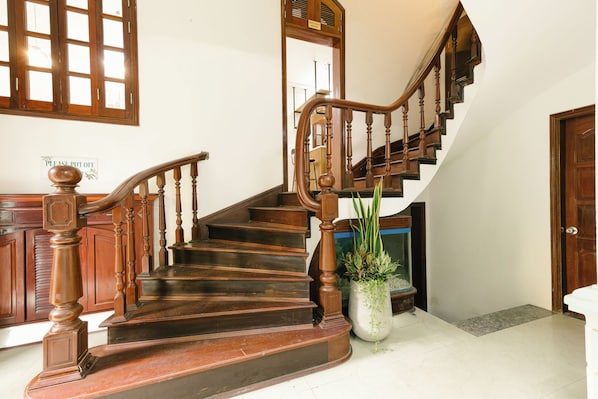 Un escalier en bois, avec une pancarte indiquant « Veuillez éteindre » et un pot de fleurs placé à côté.