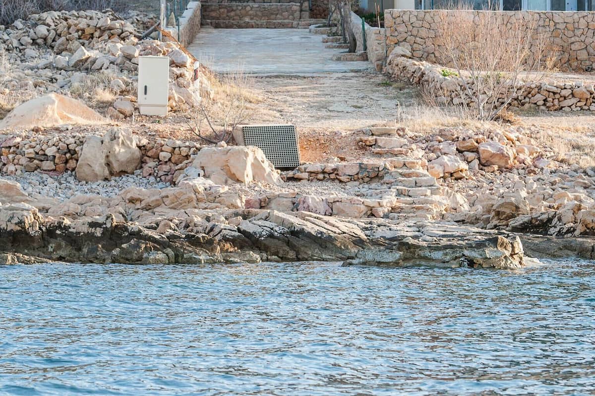Une propriété située sur la côte, avec un chemin de pierre menant à un bâtiment doté d’un toit en tuiles, et qui se trouve en bord de mer.