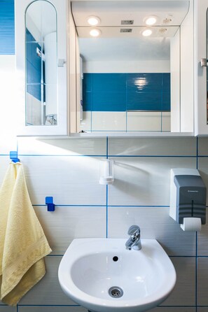A bathroom with a white sink, a mirror, a towel rack with a yellow towel, a soap dispenser, and blue-tiled walls.
