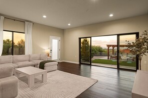 Un salon moderne avec un canapé d’angle, une table basse et une vue sur le jardin à travers de grandes portes-fenêtres coulissantes.