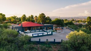Une maison moderne avec un toit rouge, une piscine et un patio entouré d’arbres.