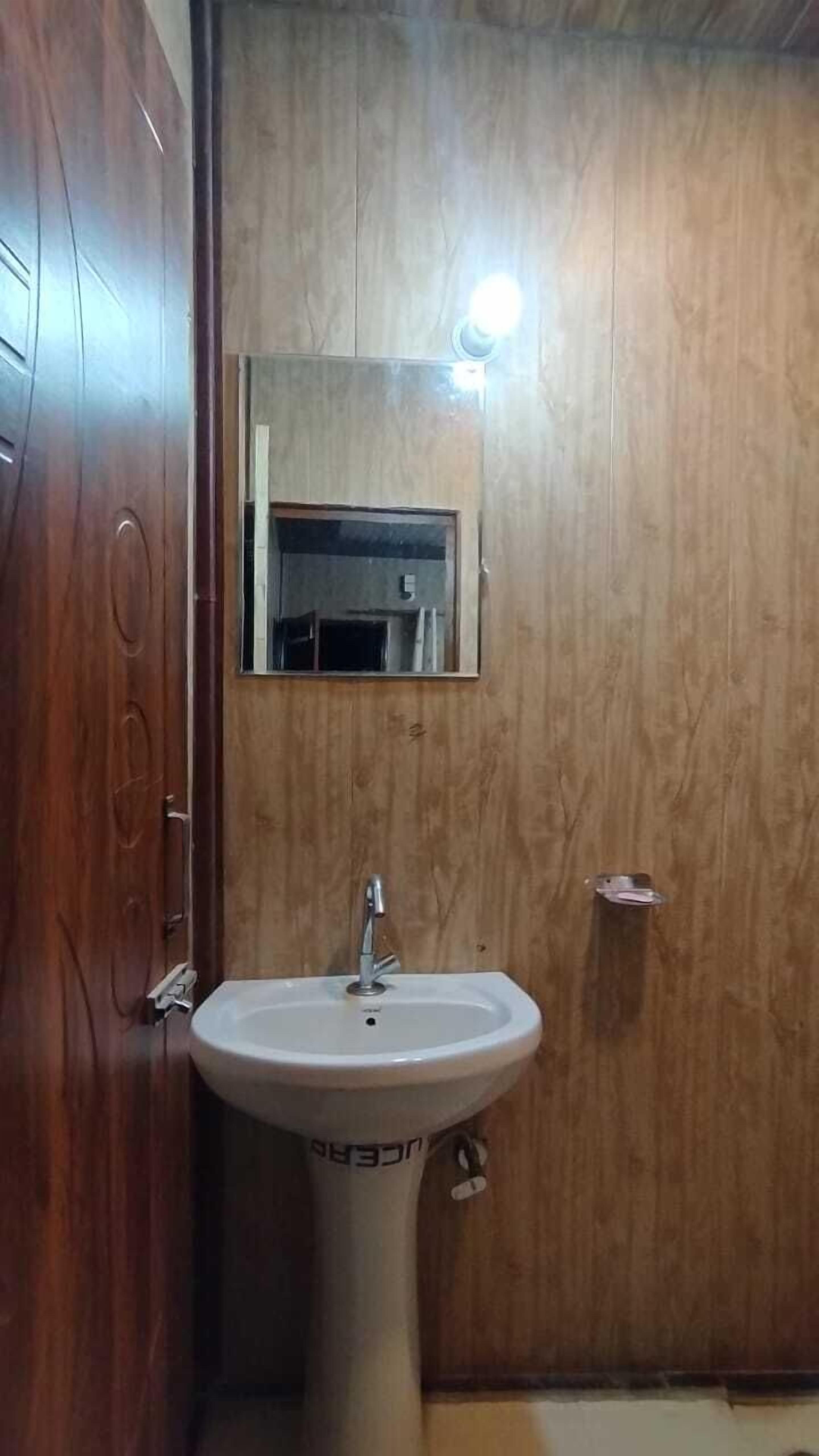A bathroom with a wooden wall, a white pedestal sink, and a mirror above it.