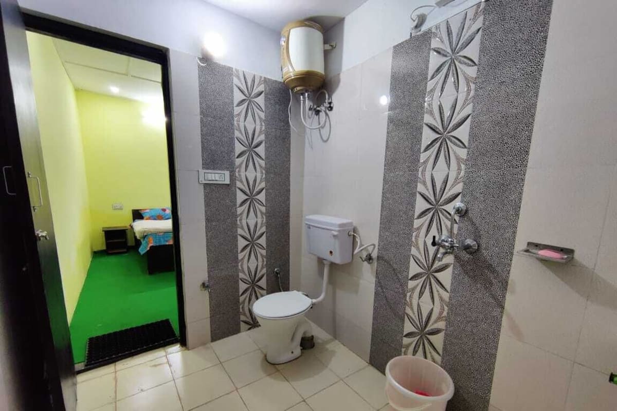 A bathroom with a toilet, a shower, and a sink. There is a bucket on the floor and a water heater mounted on the wall.