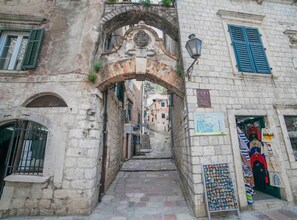 Una calle estrecha con un arco de piedra, tiendas a ambos lados y una pequeña exhibición de recuerdos frente a una tienda.