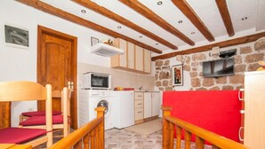A compact kitchen with a washing machine, a microwave, and a stone wall. - Cozy Stay in Kotors Old Town (Kotor)
