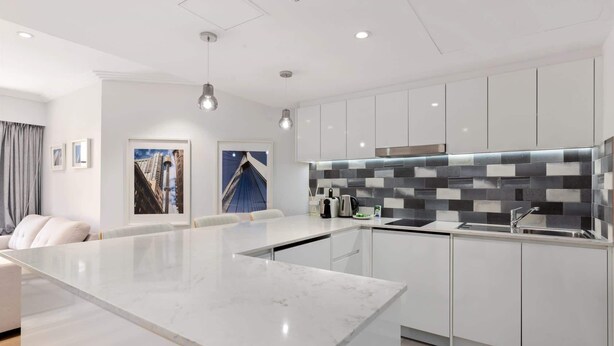 A modern kitchen with white cabinets, a marble countertop, and a backsplash with black and gray tiles. - Bright & Spacious 1-Bed in Vibrant Sydney (Sydney)