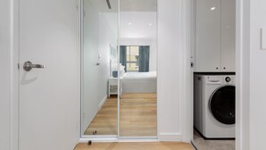 A hotel room with a sliding glass door leading to a bedroom, a washing machine, and a small bedside table. - Bright & Spacious 1-Bed in Vibrant Sydney (Sydney)