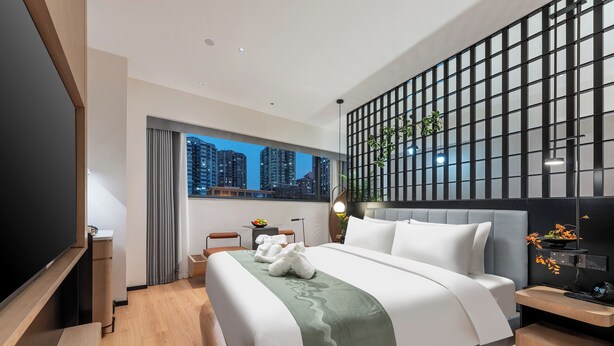 A modern hotel room with a large bed, a TV, a desk with a lamp, and a city view. - K.Space KaiShi hotel (Guangzhou)