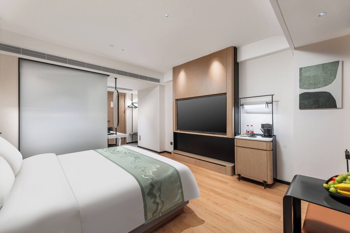 A modern hotel room with a large bed, a desk, a flat-screen TV, and a minibar.