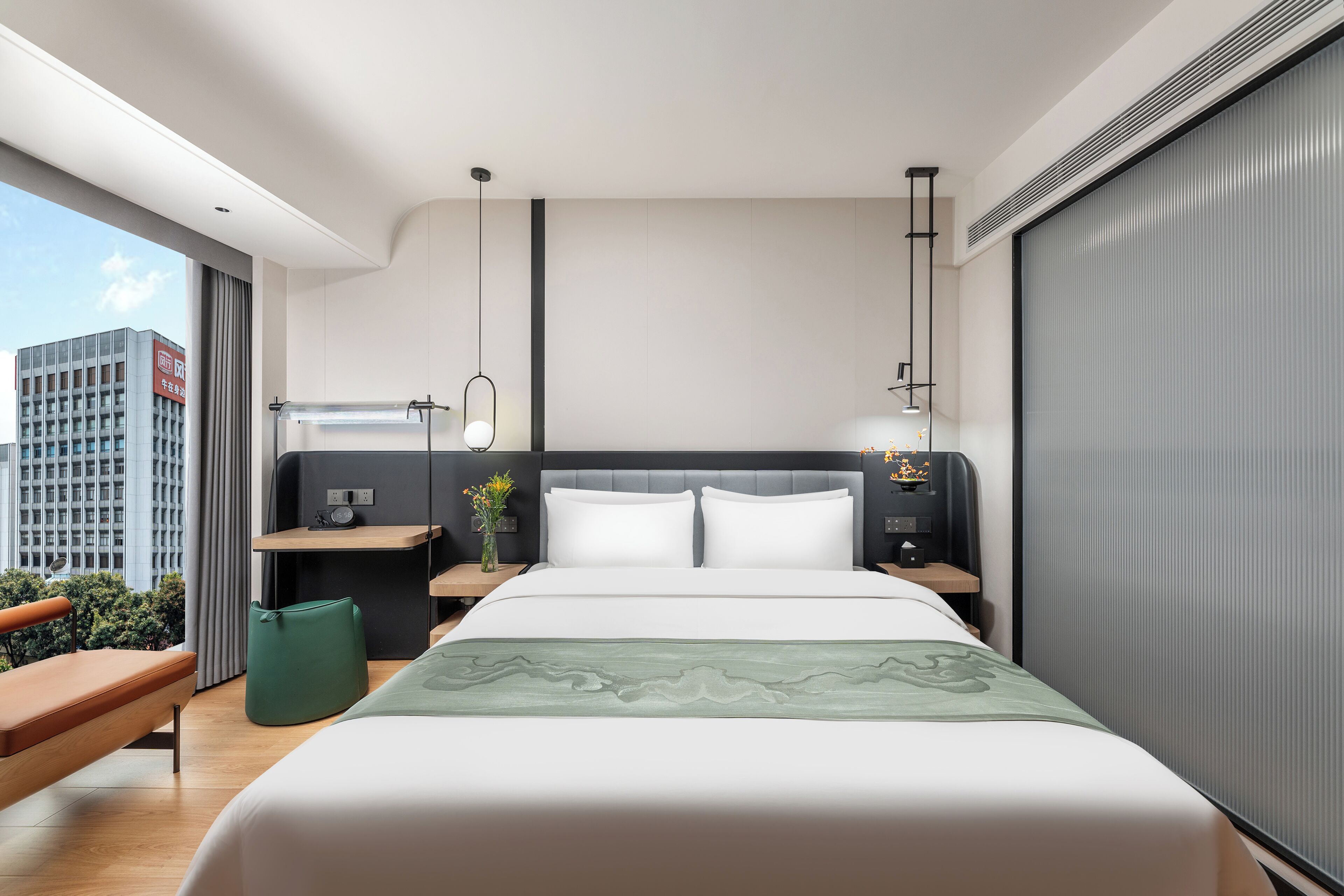 A modern hotel room with a large bed, a nightstand, a desk, and a view of the city.