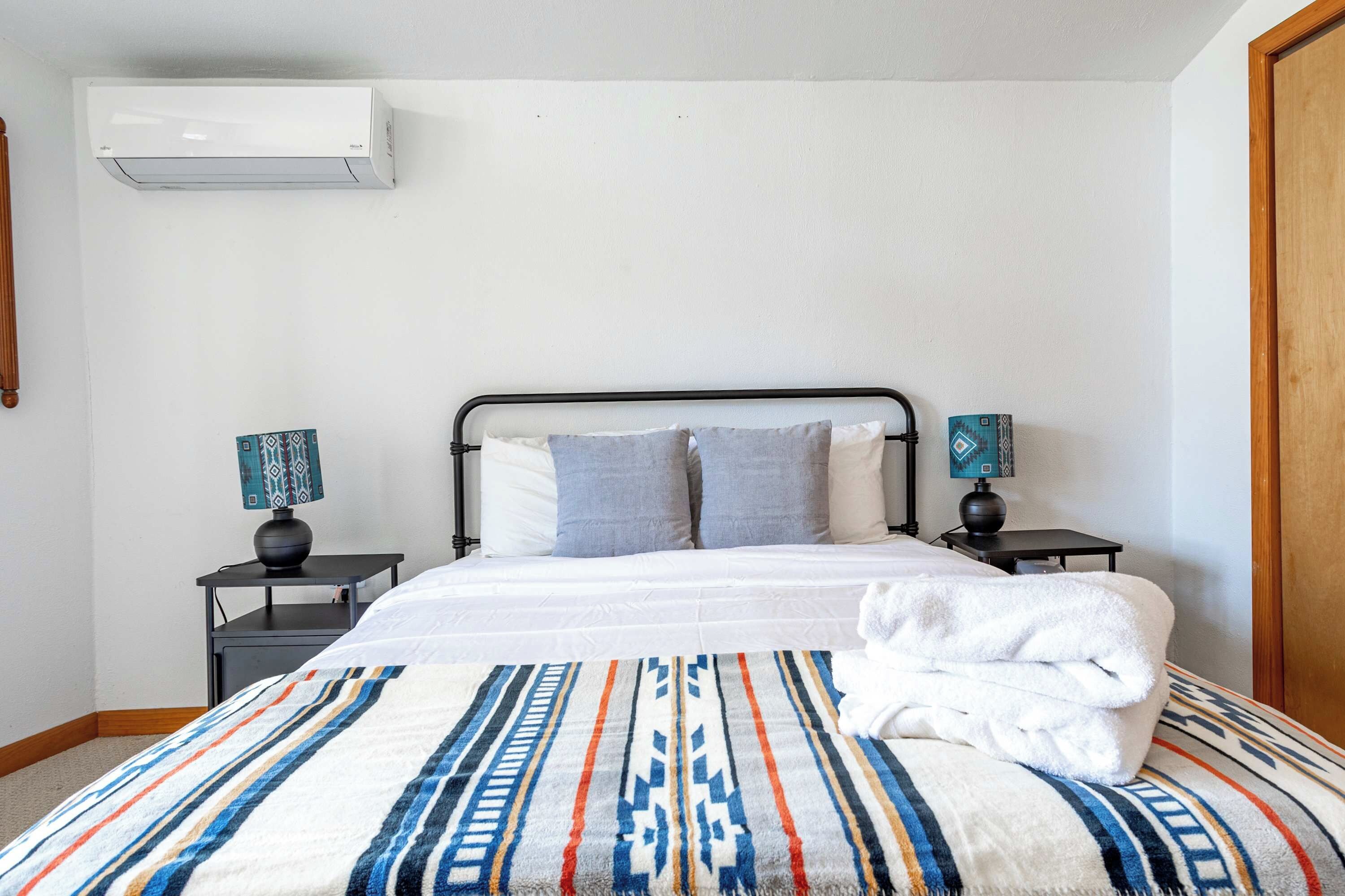 Een opgemaakt bed met een geborreld deken, twee nachtkastjes met lampen en een wandairconditioner.