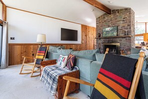 Ein gemütliches Wohnzimmer mit Kamin aus Stein, Holzmöbeln und einem an der Wand befestigten Fernseher.