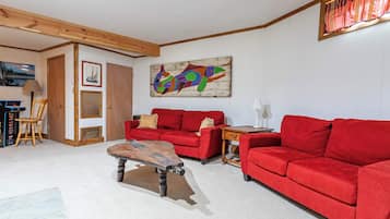 A living room with a red sofa, a wooden coffee table, and a colorful abstract painting on the wall.