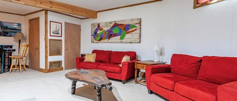 Un salon avec un canapé rouge, une table basse en bois et un tableau abstrait aux couleurs vives accroché au mur.