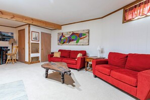 A living room with a red sofa, a wooden coffee table, and a colorful abstract painting on the wall. - Hidden Treasure Chalet Hot Tub | Game Room (Pocono Pines)
