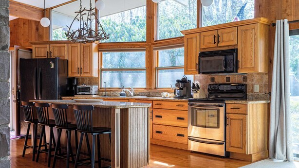 A spacious kitchen with wooden cabinets, a large island with bar stools, a built-in oven, and a microwave. - Hidden Treasure Chalet Hot Tub | Game Room (Pocono Pines)