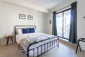 Ein ordentlich eingerichtetes Schlafzimmer mit einem Bett, einem kleinen Nachttisch, einem Sessel und einem Fenster mit Vorhängen.