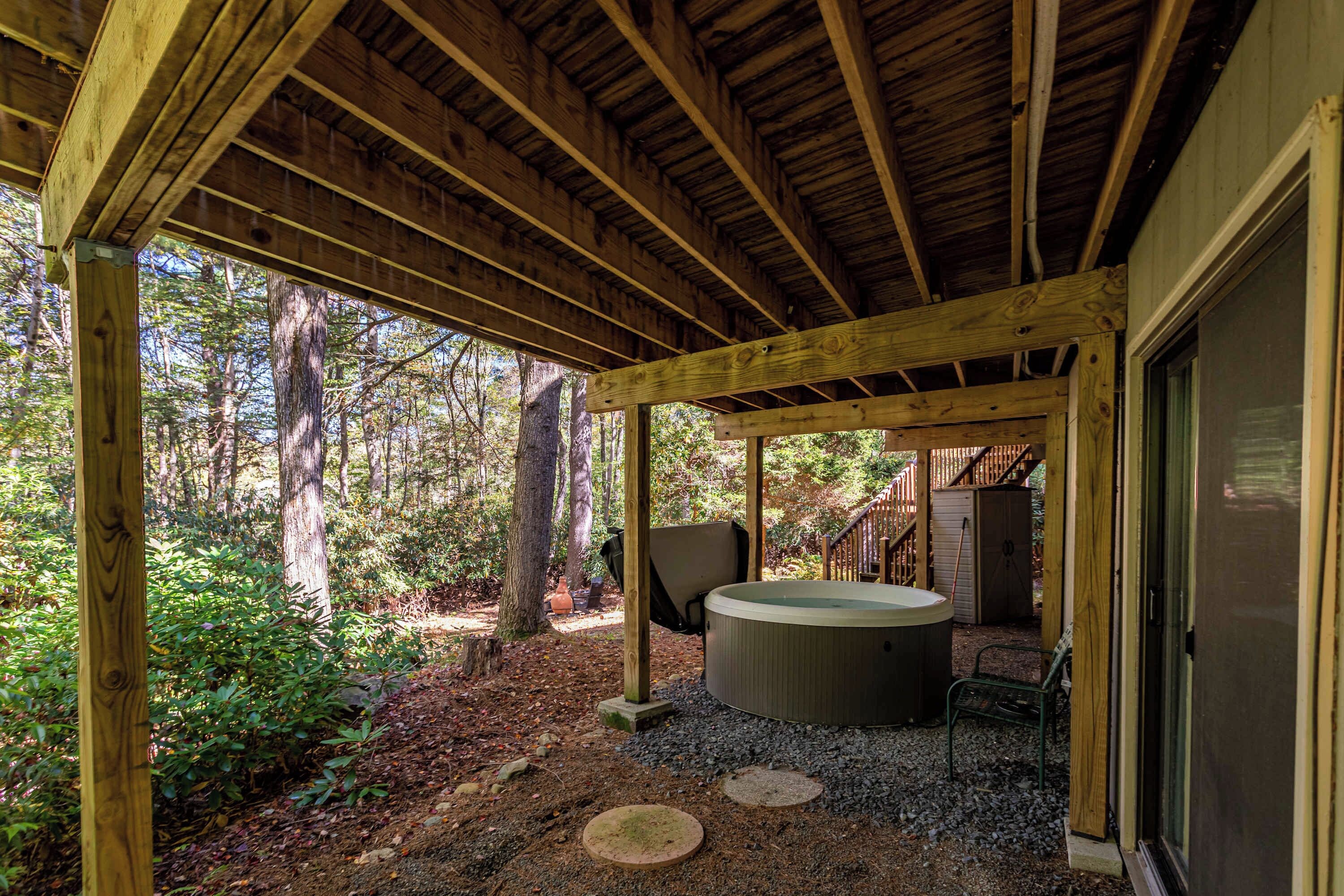 Una terraza de madera con un jacuzzi, rodeada de árboles y un sendero de grava.