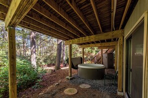 Una terraza de madera con un jacuzzi, rodeada de árboles y un sendero de grava.