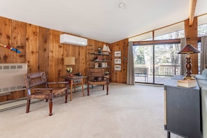 A cozy living room with wooden walls, a fireplace, a bookshelf, and a large sliding glass door leading to an outdoor deck.