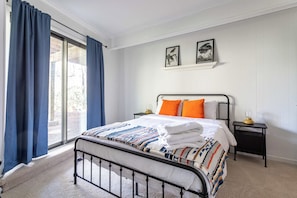 A bedroom with a bed, a nightstand, a window with curtains, and two framed pictures on the wall.