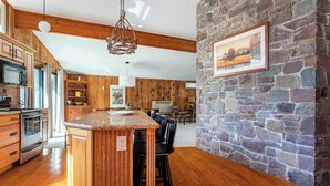 A kitchen with wooden cabinets, a granite countertop, and a stone wall. - Hidden Treasure Chalet Hot Tub | Game Room (Pocono Pines)