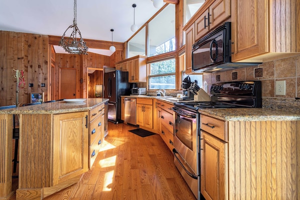 A spacious kitchen with wooden cabinetry, stainless steel appliances, and large windows allowing natural light.