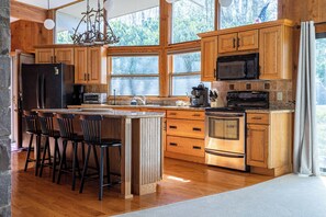 A spacious kitchen with wooden cabinets, a large island with bar stools, a built-in oven, and a microwave.