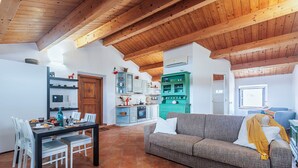 A spacious living area with a wooden ceiling, a dining table with chairs, a sofa, and a kitchen in the background.