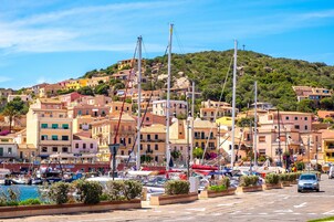 Una cittadina costiera con edifici colorati, un porto turistico con barche e una collina sullo sfondo.